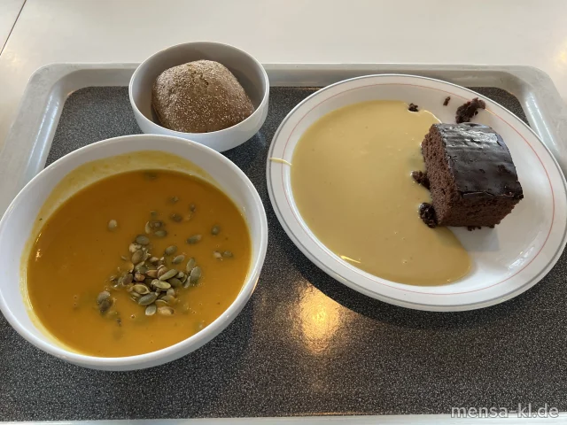 Große Portion Kürbiscremesuppe mit gerösteten Kürbiskernen (Gl), dazu ein Brötchen (Gl) und ein Stück veganer Schokokuchen (Gl) mit Mandel-Vanillesoße (Gl,Nu)