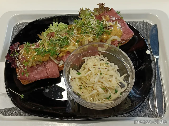 Geröstetes Dinkelbrot belegt mit Pastrami (geräuchertes Rindfleisch), Kräuterquark, Gewürzgurke und Honig-Senf-Soße (1,5,9,La,Sw,Sf,R), dazu ein Krautsalat